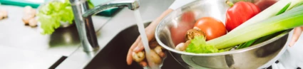 En kock på en restaurang sköljer grönsaker under rinnande vatten
