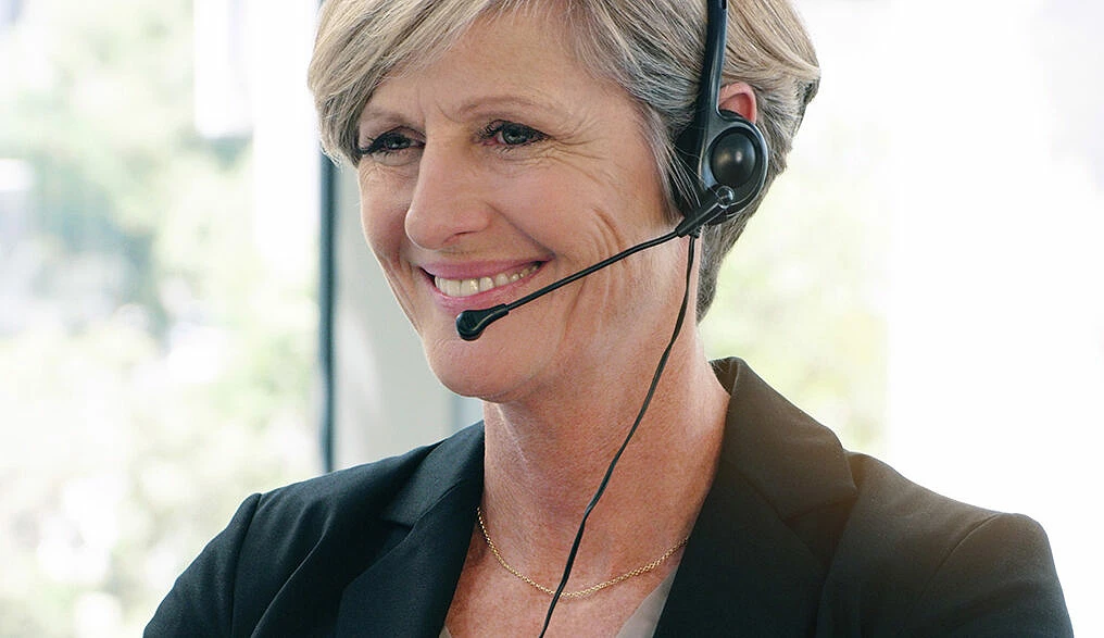 Kvinna sitter med headset och pratar i telefonen framför en dator