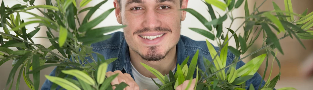 Ung man tittar fram bland gröna växter