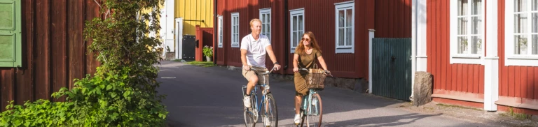 En man och en kvinna som cyklar på en gata bland röda gamla hus