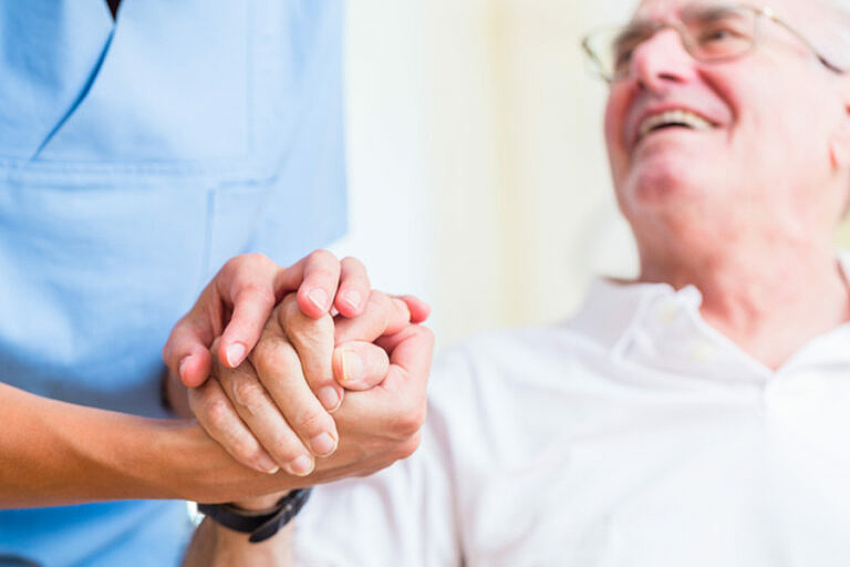 Sköterska håller handen på en äldre man