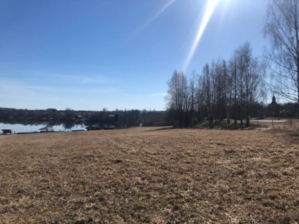 Bild på planområdet. Åkermark med älven och lövträd i bakgrunden.
