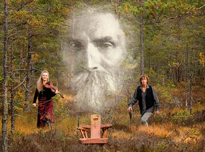 En fantasifull bild på två musiker i en skog. de håller i sina instrument och i samma bild syns ett stort ansikte av en man med skägg. ansiktet är transparent och svartvitt som på ett gammalt foto och är skapt som en extra effekt, som för att påminna och svunna tider och människor