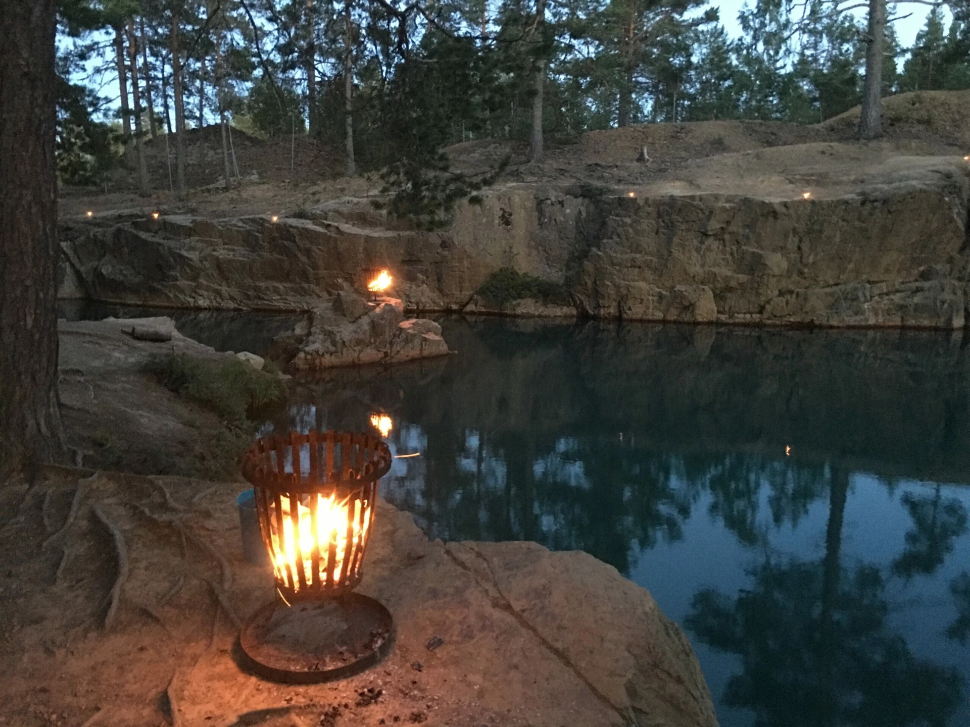 Bilden föreställer det spegelblanka vattnet vid gruvhålet vid Östra Silvbergs Gruva. Eldar och marschaller lyser upp i skymningsljuset.