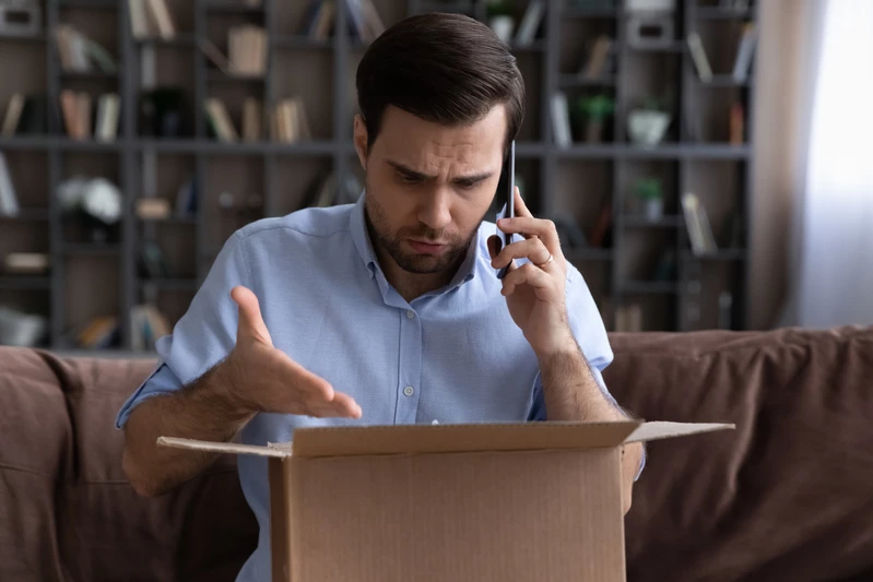 Besviken man som har öppnat ett paket. Ringer konsumentvägledningen.