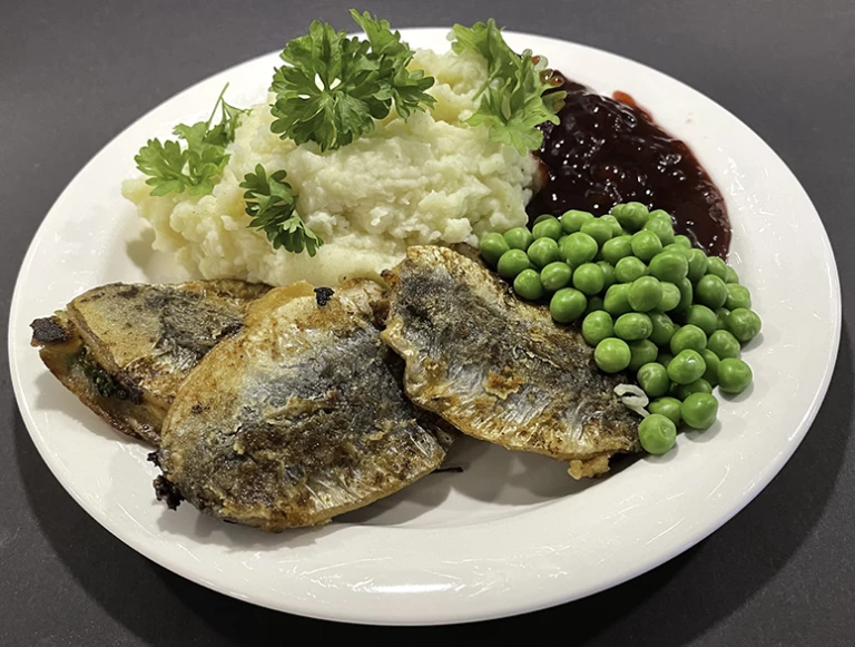 En tallrik med strömming, potatismos, ärter och lingonsylt.