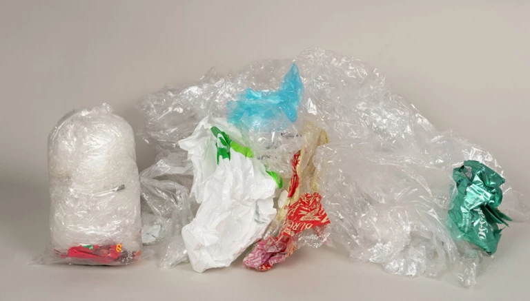 En mindre påse är fylld med mjukplast när man har använt Minimizern, bredvid en hög med lös mjukplast.