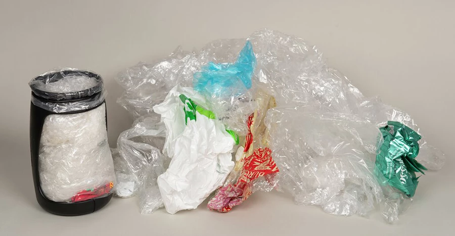 En Minimizer där det sitter en mindre påse fylld med mjukplast, bredvid en hög med lös mjukplast.
