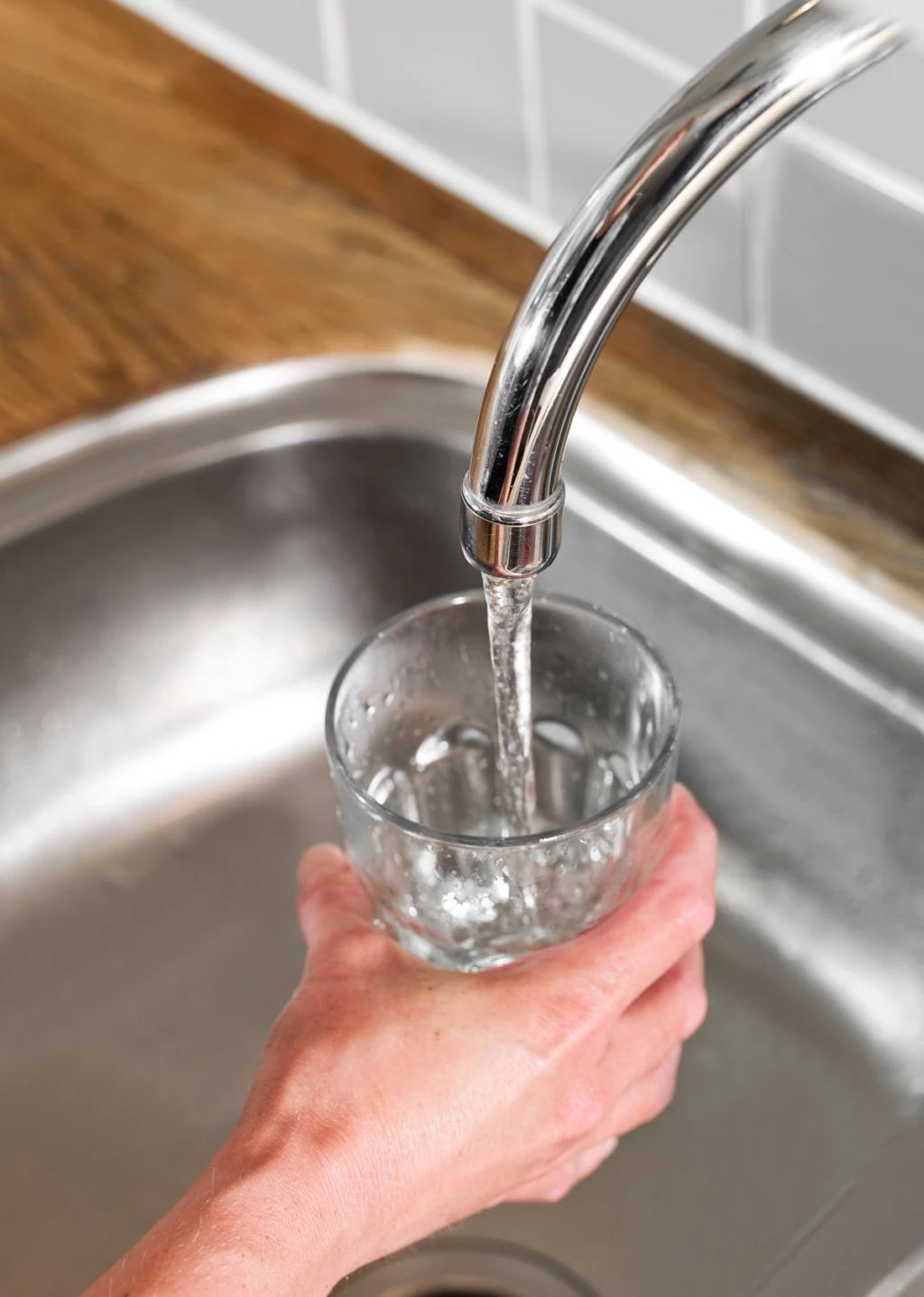En hand som håller i ett glas och fyller det med vatten från kranen