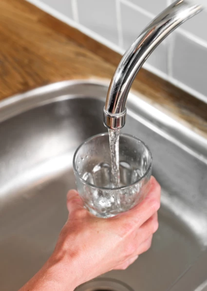 En hand som håller i ett glas och fyller det med vatten från kranen