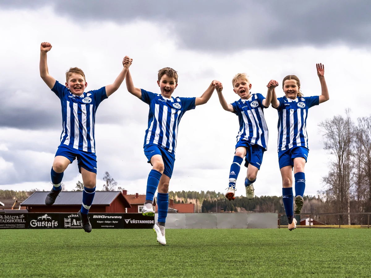 Fyra fotbollsspelare hoppar hand i hand upp i luften
