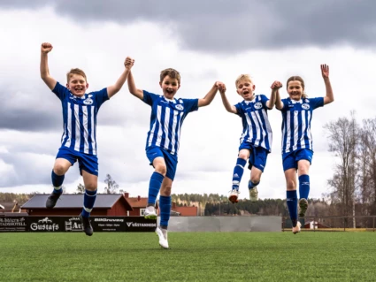 Fyra fotbollsspelare hoppar hand i hand upp i luften