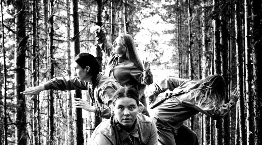 Bilden är svartvit och föreställer 4 stycken samiska kvinnor i en skog. En av kvinnorna tittar rakt in i kameran, de andra åt sidorna.