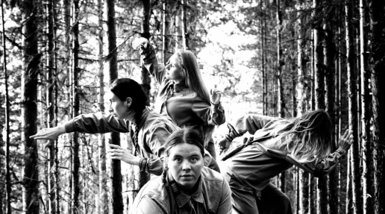 Bilden är svartvit och föreställer 4 stycken samiska kvinnor i en skog. En av kvinnorna tittar rakt in i kameran, de andra åt sidorna.