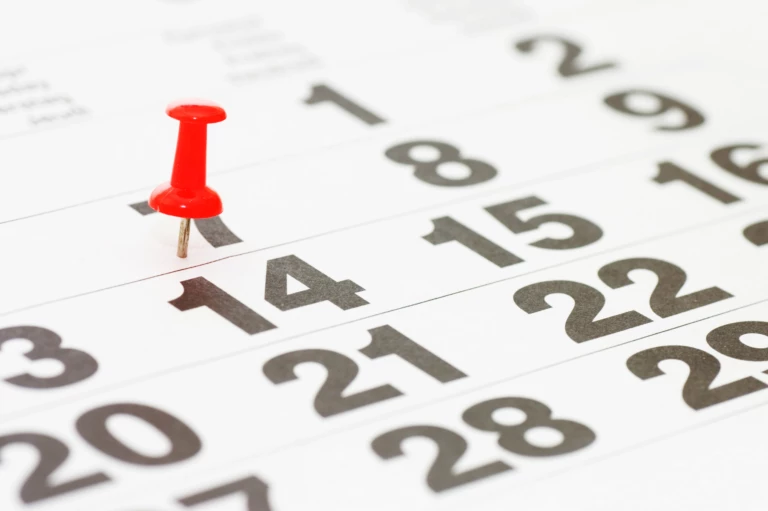 Kalender med datum och ett rött häftstift fastsatt på ett av datumen