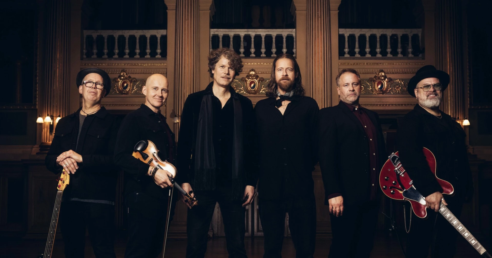 Bilden är en bild på alla medlemmar i bandet Engmans Kapell. De står bredvid varandra med sina musikinstrument i handen och tittar in i kameran.