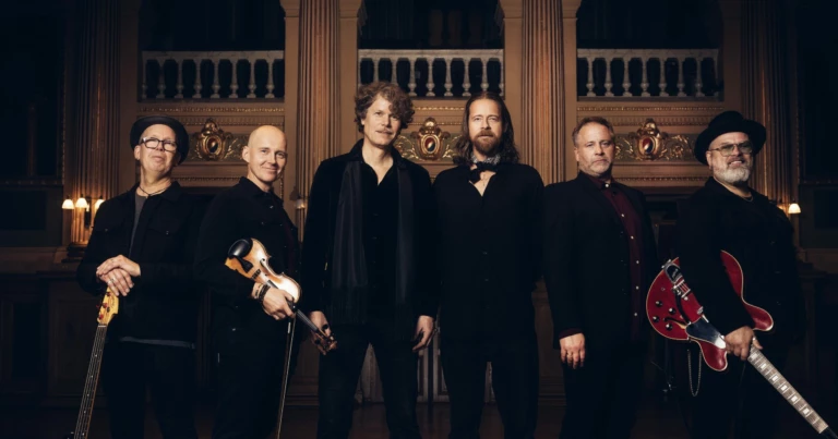 Bilden är en bild på alla medlemmar i bandet Engmans Kapell. De står bredvid varandra med sina musikinstrument i handen och tittar in i kameran.