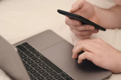 händer som håller i en mobiltelefon och en laptop