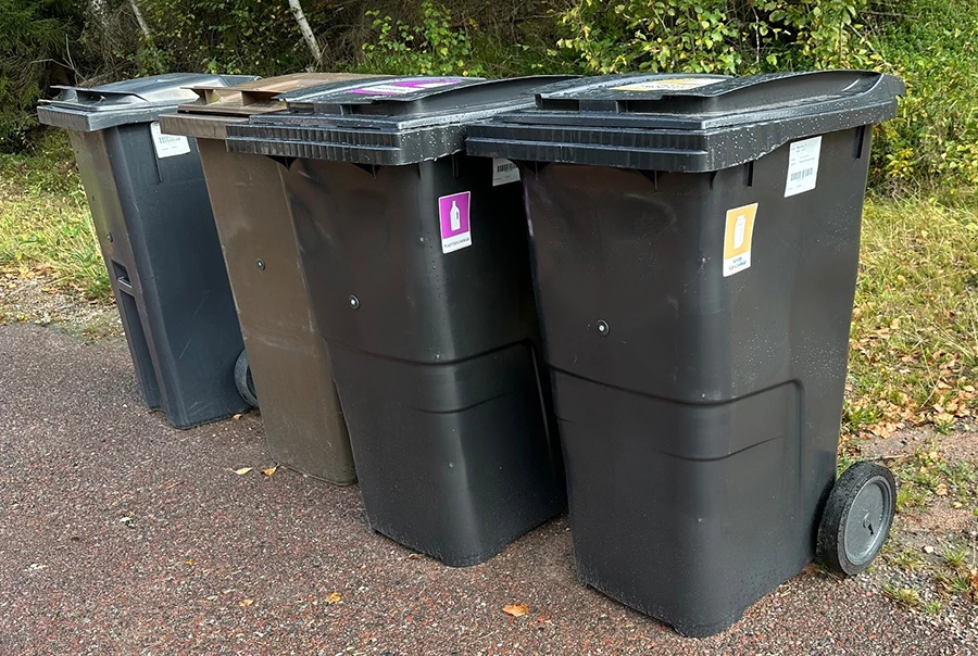 fyra soptunnor på en rad längs en väg en höstdag