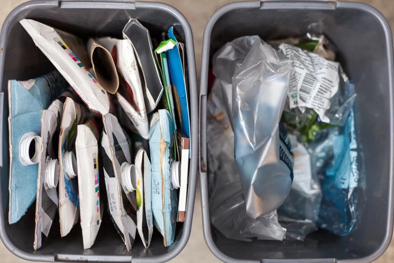 Två avfallshinkar, den ena fylld med pappersförpackningar och den andra med plastförpackningar.