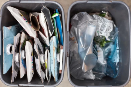 Två avfallshinkar, den ena fylld med pappersförpackningar och den andra med plastförpackningar.