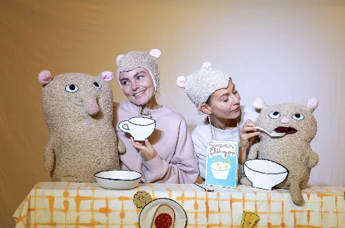 En bild på två skådespelare utklädda till björnar som matar två teddybjörnar vid ett matbord