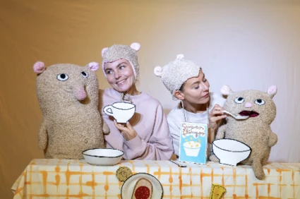 En bild på två skådespelare utklädda till björnar som matar två teddybjörnar vid ett matbord