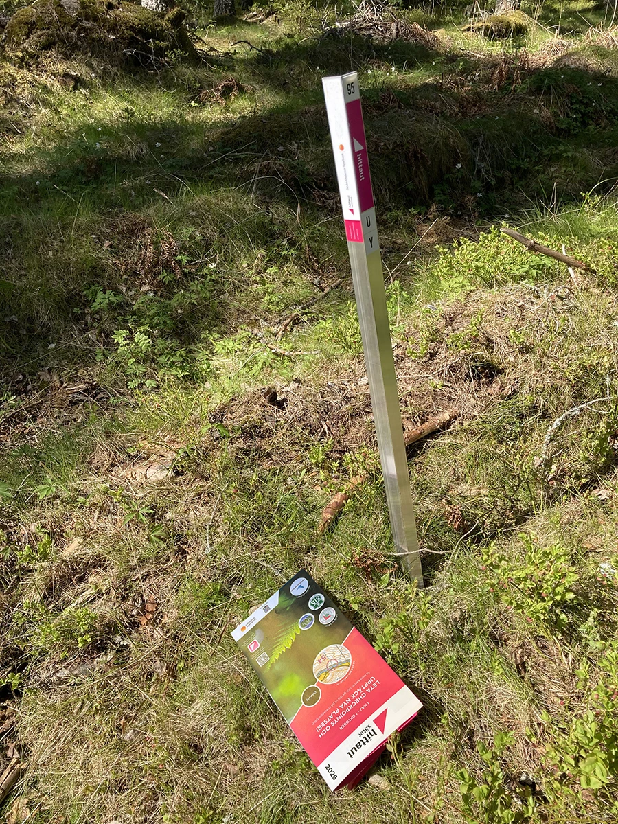 en hittautstolpe i naturen och en papperskarta som ligger bredvid på marken