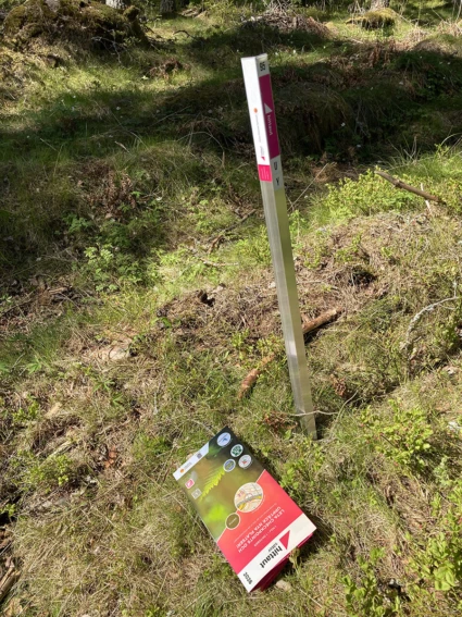 en hittautstolpe i naturen och en papperskarta som ligger bredvid på marken