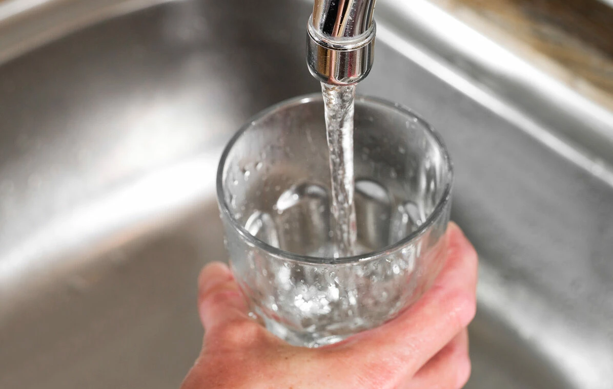 En person håller i ett glas och fyller på med vatten från en kran