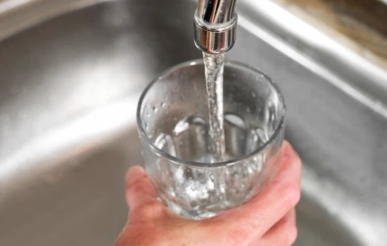 En person håller i ett glas och fyller på med vatten från en kran