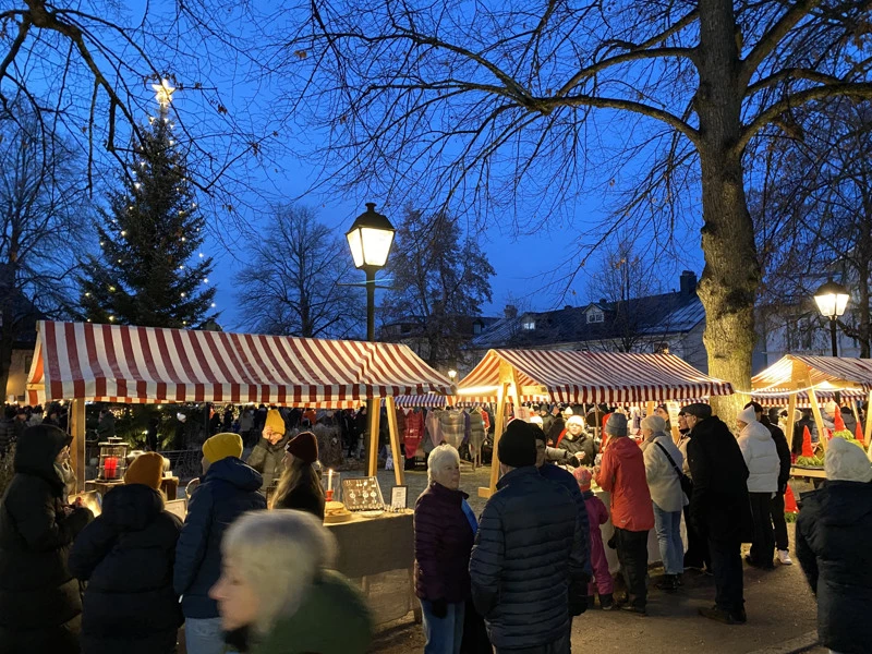 Julmarknad med marknadsstånd med julgranen i bakgrunden.
