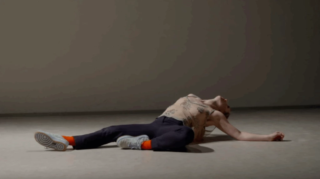 En scenbild ur Dansföreställningen Ranunculus. Dansaren ligger på rygg på scenen, stödd med armbågarna och bakåtlutat huvud