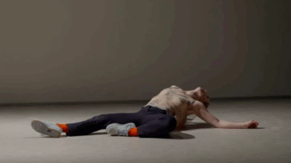 En scenbild ur Dansföreställningen Ranunculus. Dansaren ligger på rygg på scenen, stödd med armbågarna och bakåtlutat huvud