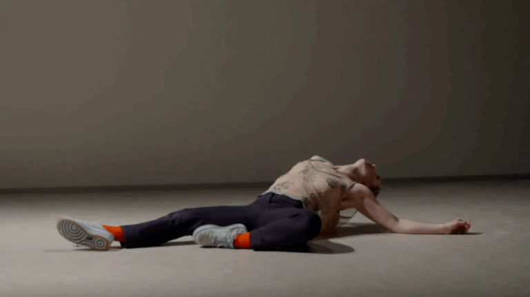 En scenbild ur Dansföreställningen Ranunculus. Dansaren ligger på rygg på scenen, stödd med armbågarna och bakåtlutat huvud