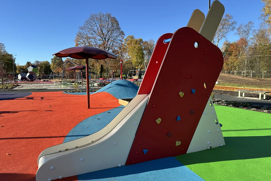 Rutschbana formad som en röd glass med pinne, omgiven av färgglada lekytor i Pep-park Säter.